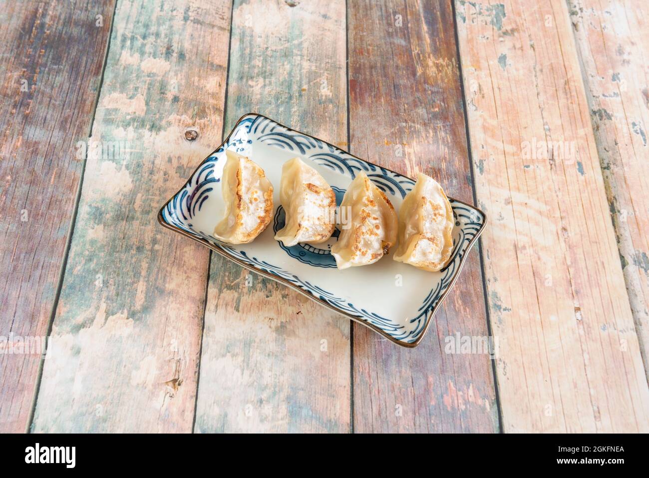Eine Portion von vier Empanadillas, Gyozas, gegrilltem Fleisch auf einem schönen Teller mit blauen Details auf einem hölzernen Hintergrund gebraten Stockfoto