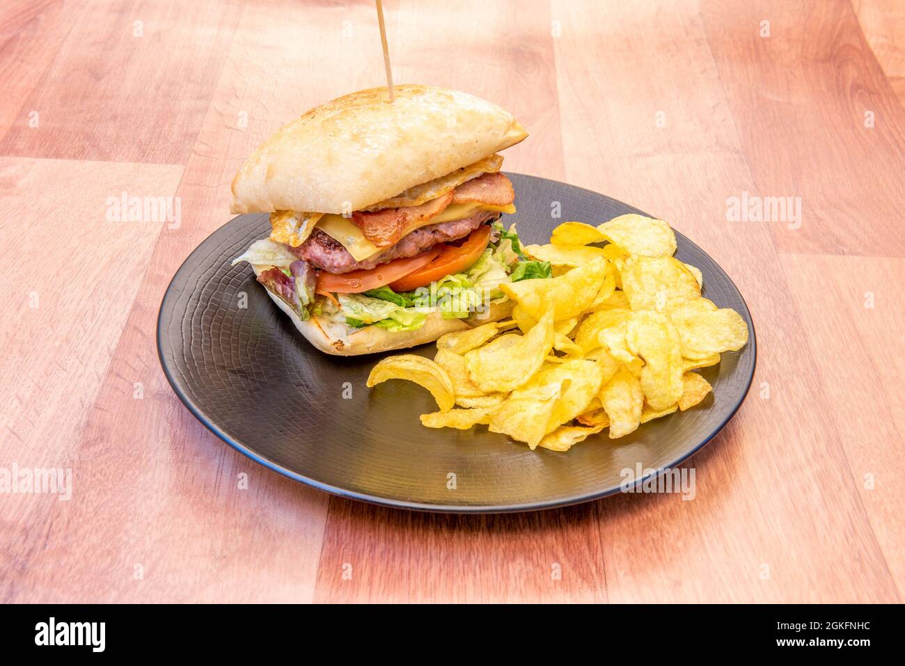 Rindfleisch-Burger mit Ei, Käse, Speck und Salat in einem rustikalen Brot und pommes auf einem schwarzen Teller Stockfoto