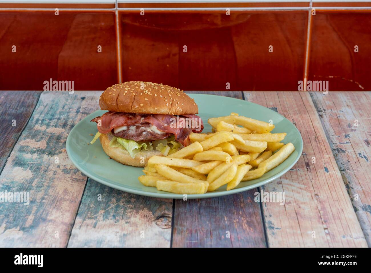 Rindfleisch-Burger mit viel Speck oben und eine große Portion Pommes auf einem blauen Teller Stockfoto