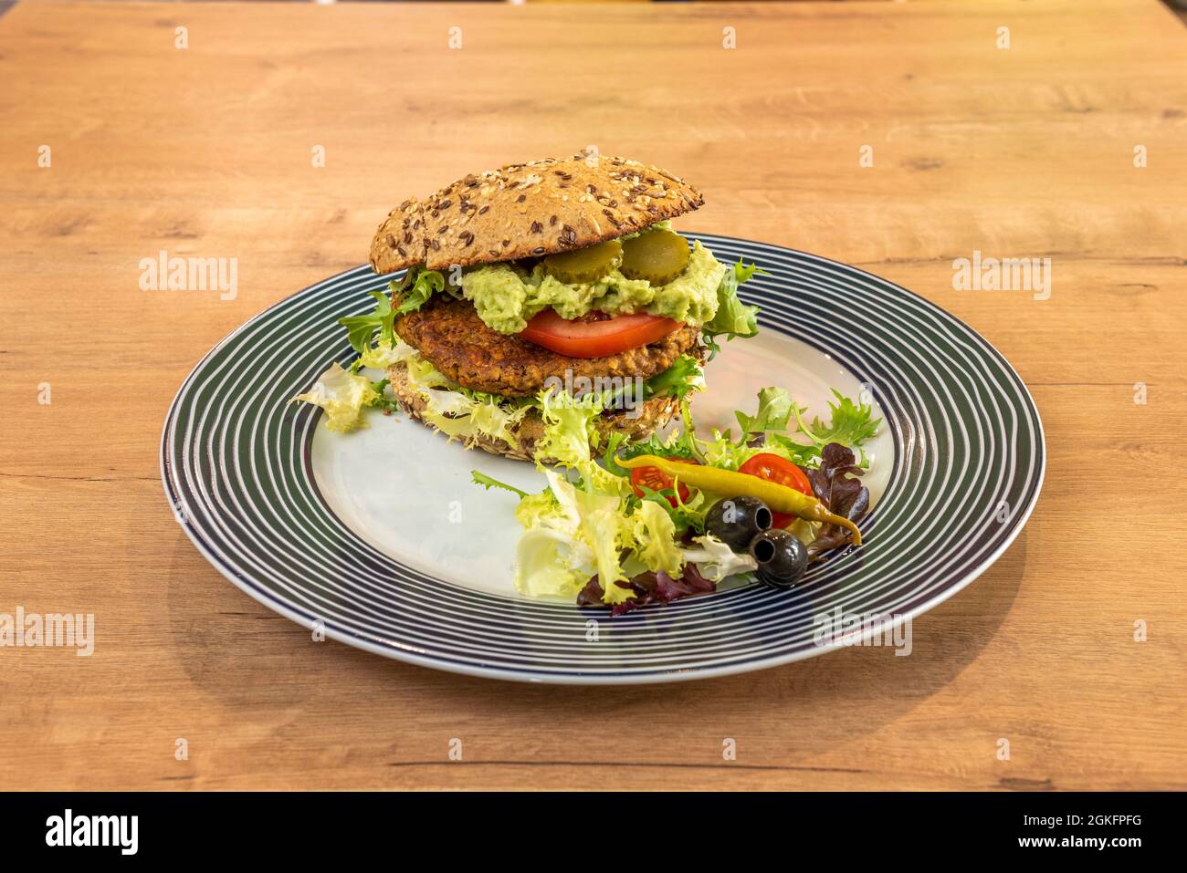 Fantastischer veganer Linsenburger mit Guacamole, Gurken, Tomaten, Salat, Piparra, Schwarze Oliven und Kirschtomaten auf einem schönen Teller Stockfoto
