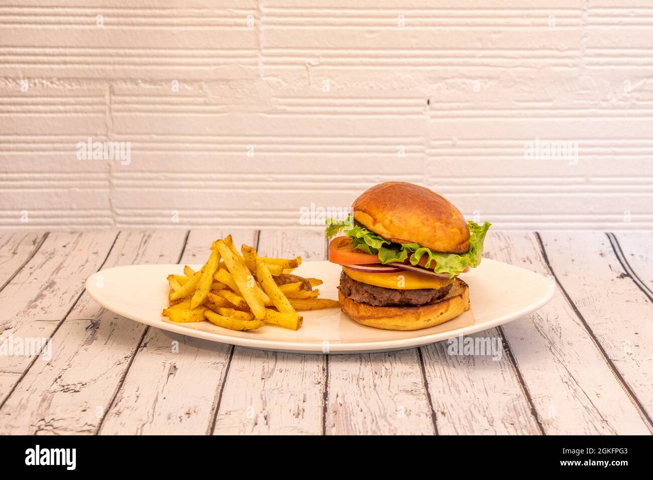 Klassischer Rindfleischburger mit roten Zwiebeln, Tomatenscheiben, Cheddar-Käse und Eisbergsalat auf einem weißen Tablett und einer Seite Pommes frites Stockfoto