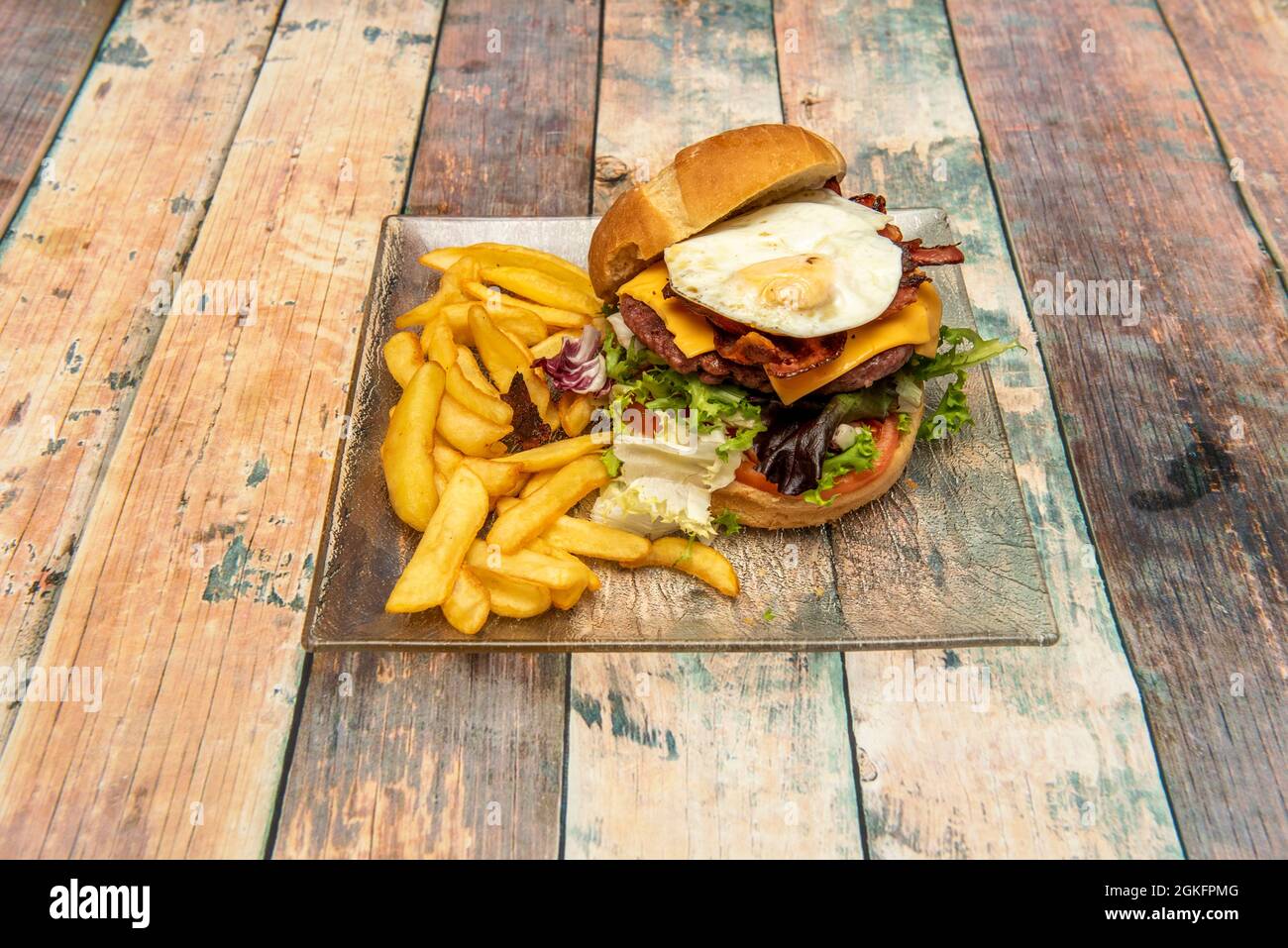 Rindfleisch-Burger mit vielen gemischten Salatsprossen, Cheddar-Käse, Spiegelei und viel Speck auf einem Glasplatte Stockfoto