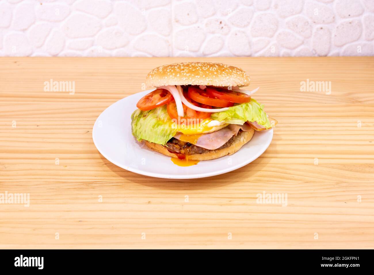 Spezieller Hamburger mit vielen Tomatenscheiben, frittiertem Eigelb auf dem Schinken und Kalbfleisch auf einem weißen Teller Stockfoto