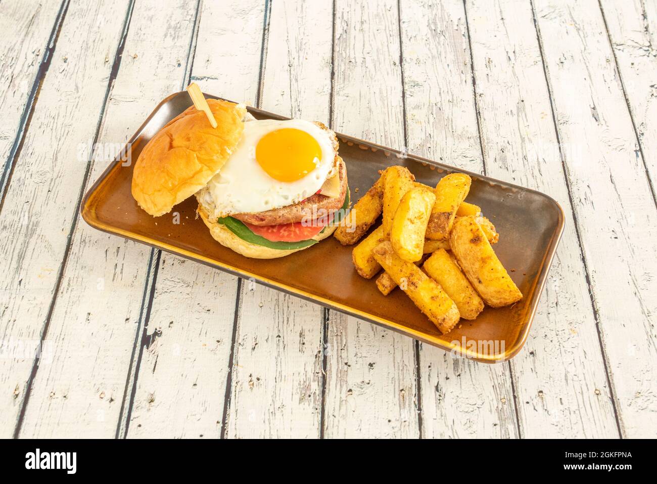 Appetitlich hausgemachter Burger mit einem Spiegelei mit glänzendem Eigelb und einer Seite von Deluxe-Pommes mit Haut Stockfoto