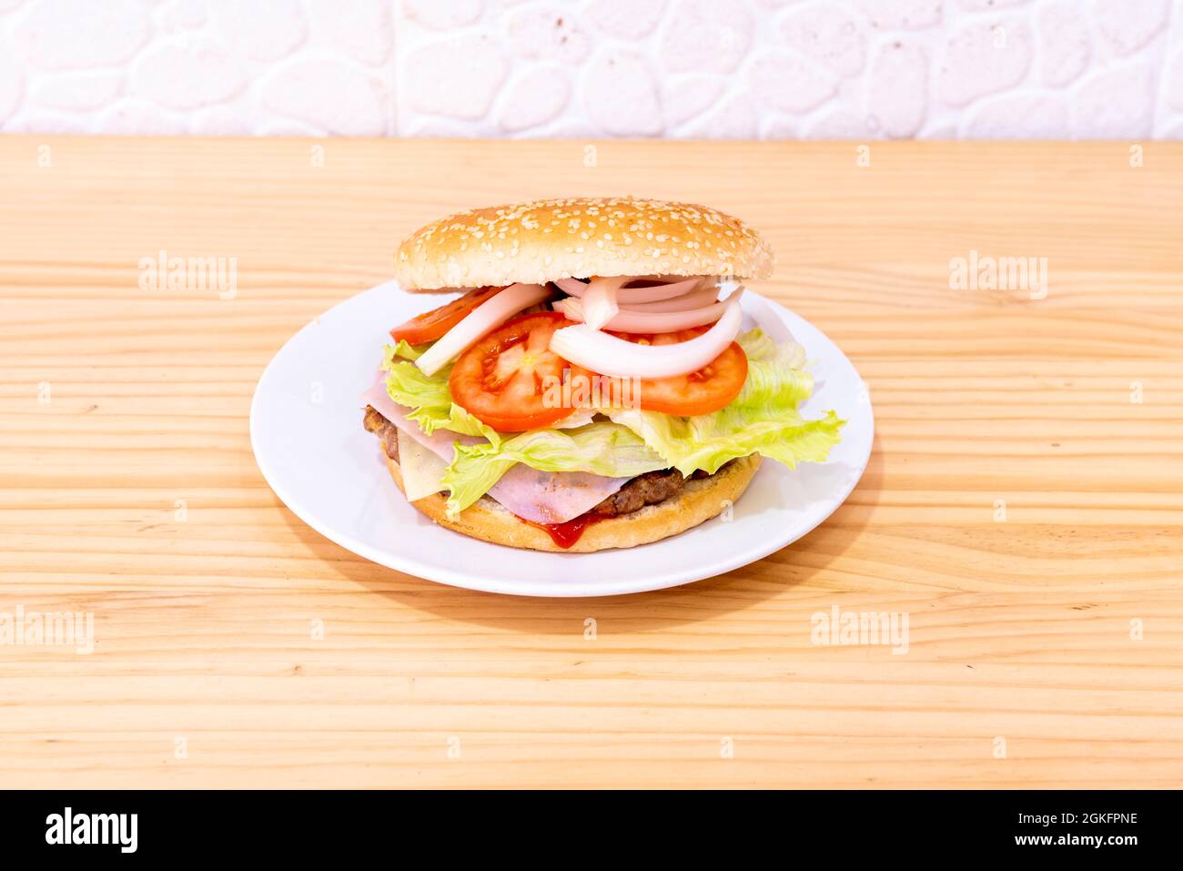 Klassischer Hamburger mit viel Tomaten, viel weißer Zwiebel, Eisbergsalat, Schinken und einer Scheibe Käse auf einem Rinderfilet Stockfoto