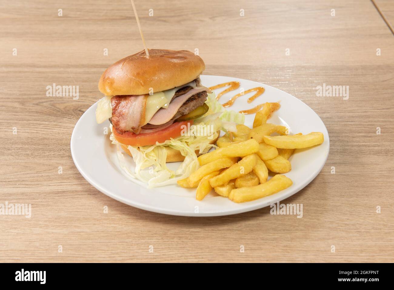 Klassischer Rindfleischburger mit Speck, Schinken, eingelegten Gurken, Tomaten und Zwiebeln und einer Seite Pommes frites Stockfoto