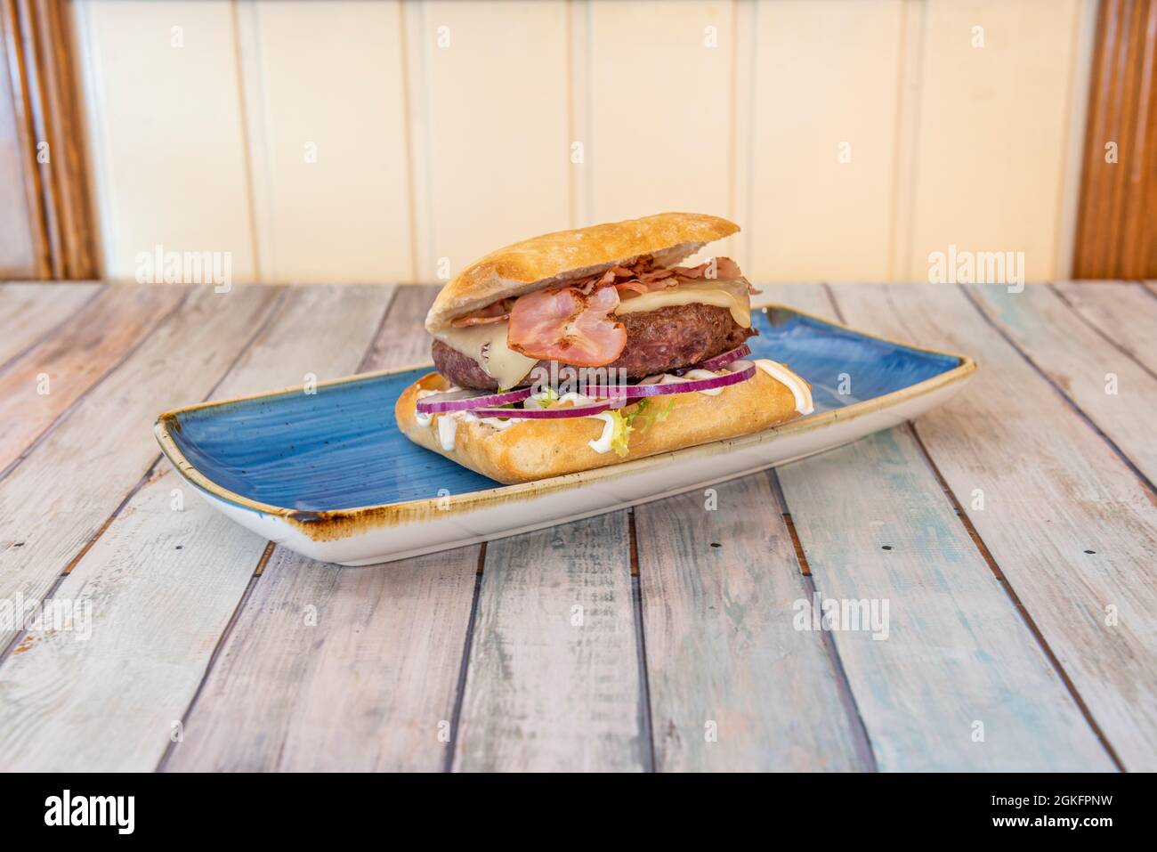 Rinderburger mit roten Zwiebeln, Käse und Speck auf blauem Teller Stockfoto