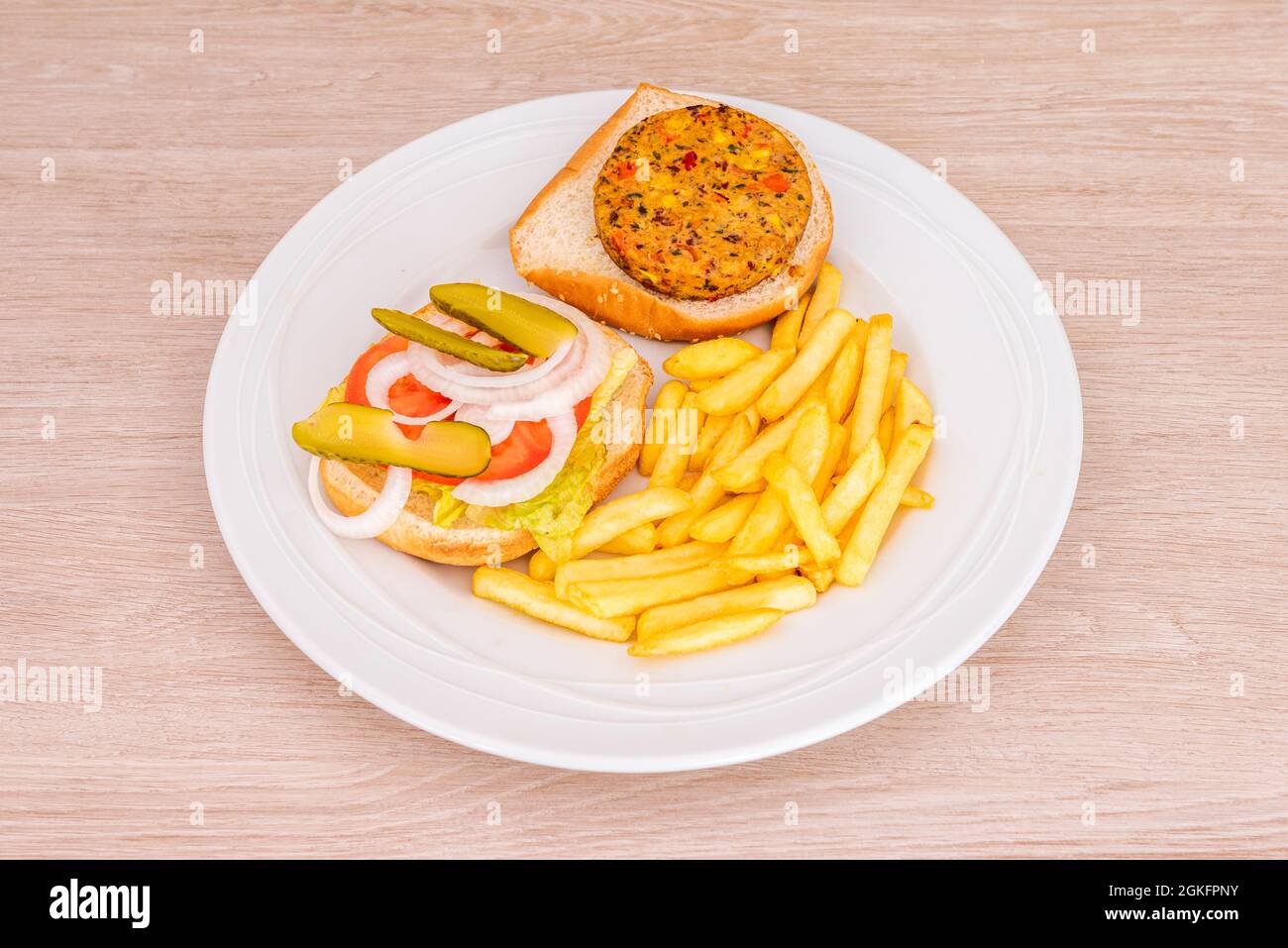 Veganer Gemüseburger mit Zwiebeln, Tomaten und eingelegten Gurken und einer Seite Pommes Frites Stockfoto
