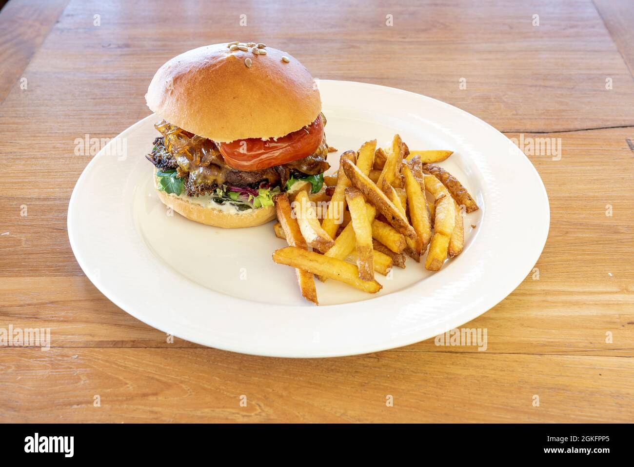 Toller Hamburger mit gebratenem Pfeffer, karamellisierten Zwiebeln, Sonnenblumenkernen, Salatsprossen und Pommes frites mit Schale auf einem Holztisch Stockfoto