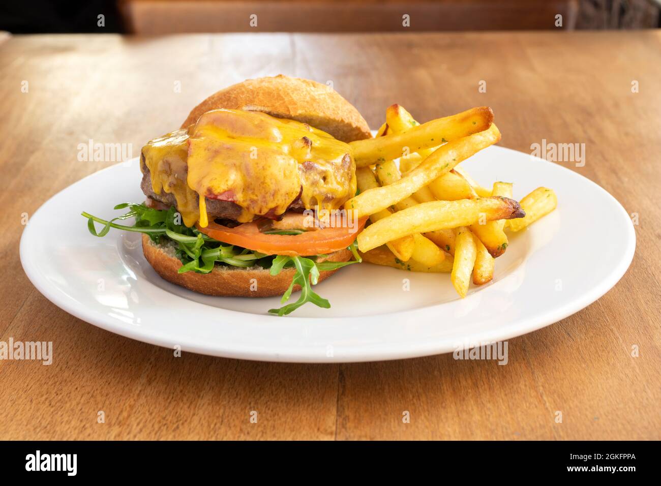 Rinderburger mit geschmolzenem Cheddar-Käse, leckeren gewürzten Pommes frites und Spezialbrot Stockfoto