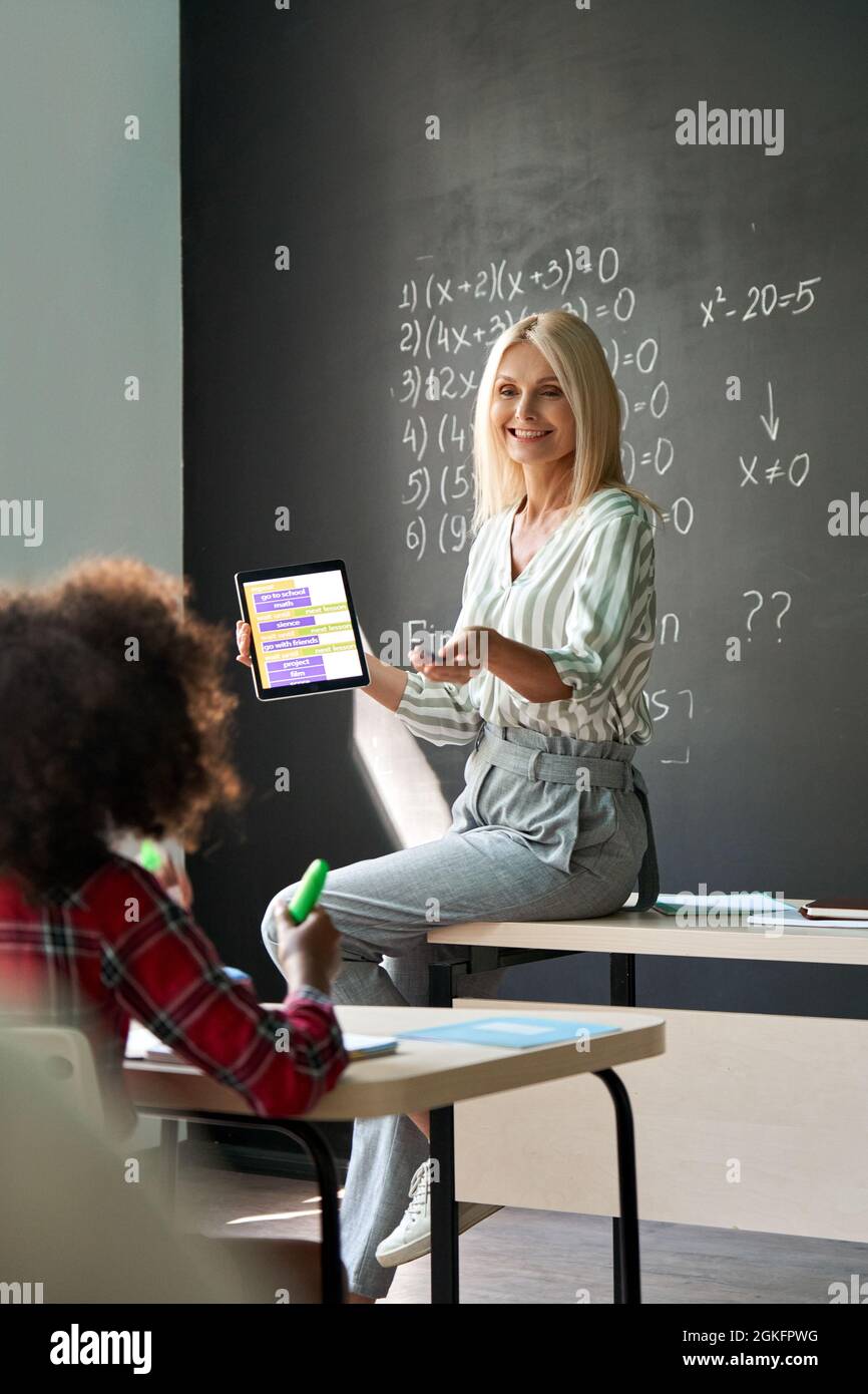 Lächelnder Lehrer, der Mathematikunterricht auf dem Schreibtisch hält und ein Tablet hält. Stockfoto