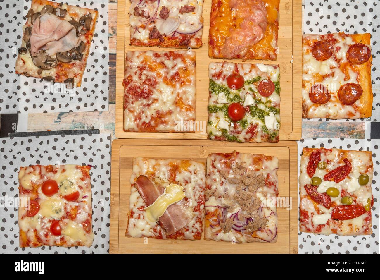 Draufsicht auf große Mengen von quadratischen Pizzateilen verschiedener Geschmacksrichtungen auf Holzbrett und Backpapier Stockfoto