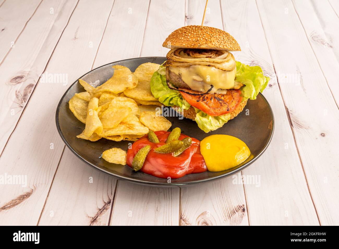 Rinderburger mit gebratener Zwiebel mit Tomaten, Salat, geschmolzenem Käse, Pommes frites, eingelegte Gurken, Ketchup und Senf Stockfoto