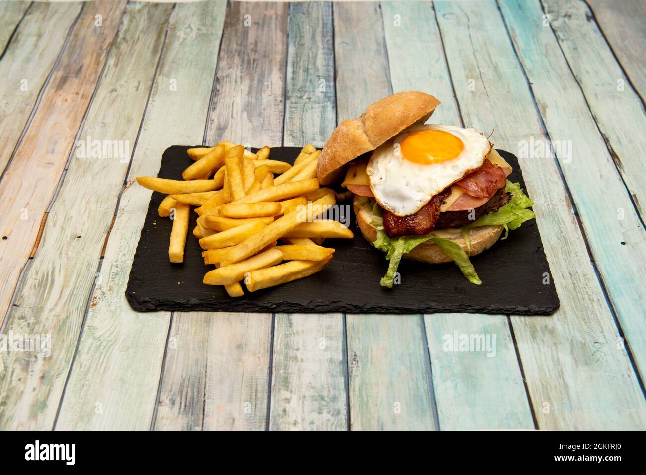 Rindfleisch-Burger mit Speck, serrano-Schinken, geschmolzenem Käse, Salat mit einem Spiegelei auf der Oberseite in rustikalem Brot Stockfoto