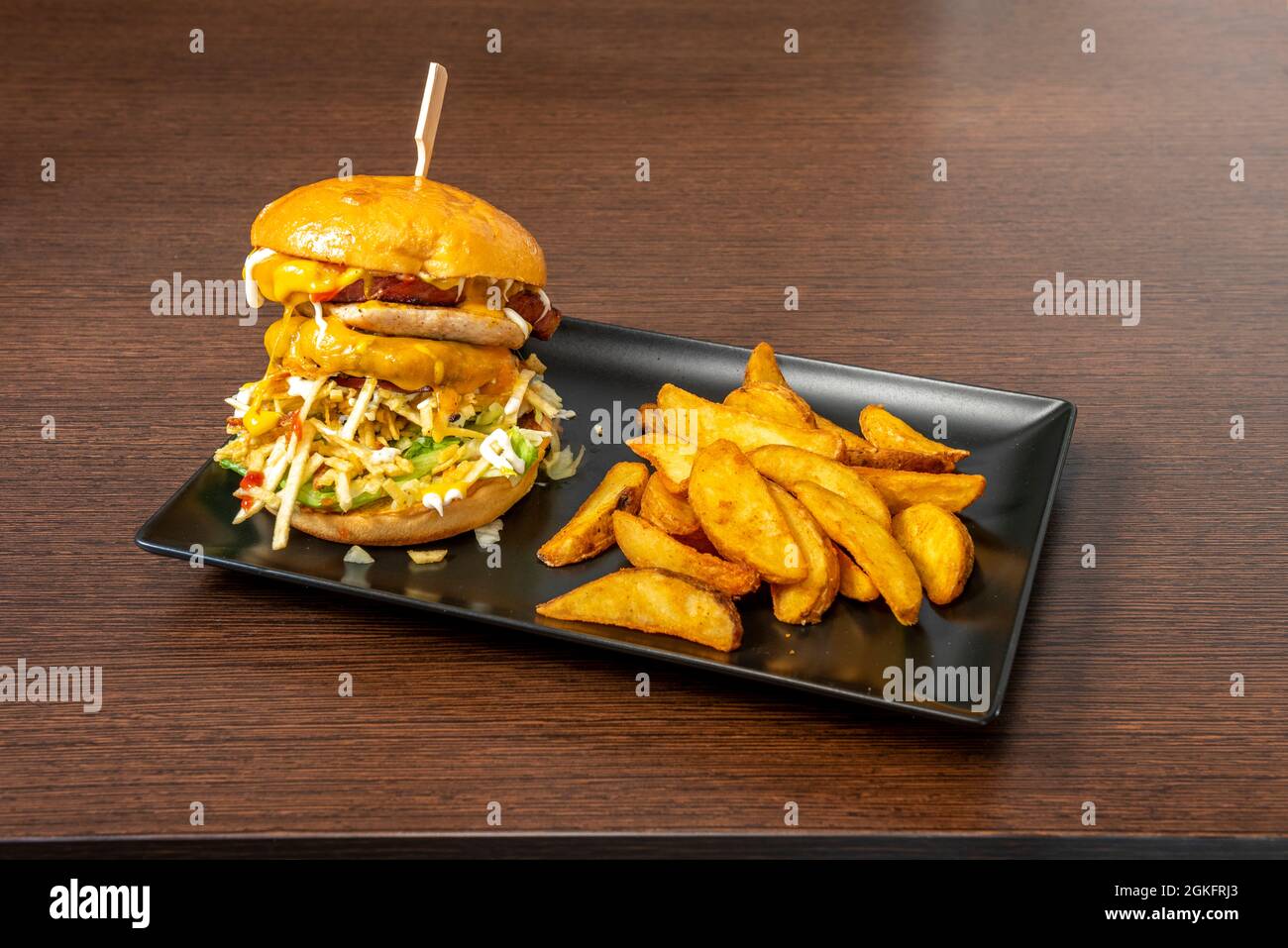 Double Burger mit viel geschmolzenem Cheddar-Käse, Strohkartoffeln, Speck, Salat, Mayonnaise, Senf und Ketchup mit einer Seite von Deluxe-Pommes Stockfoto