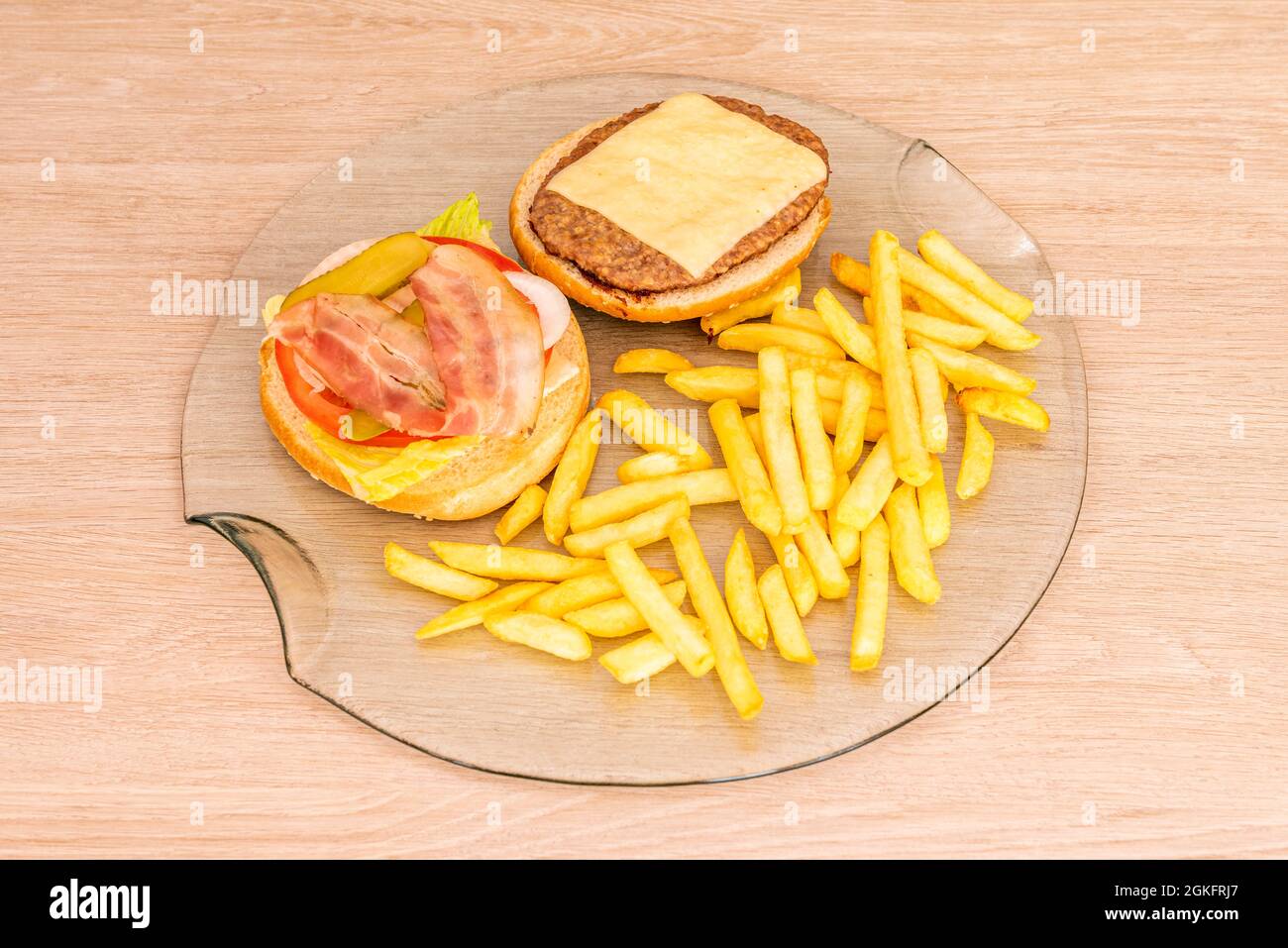 Der klassische Hamburger wird offen auf einer transparenten Glasplatte mit Pommes frites präsentiert Stockfoto