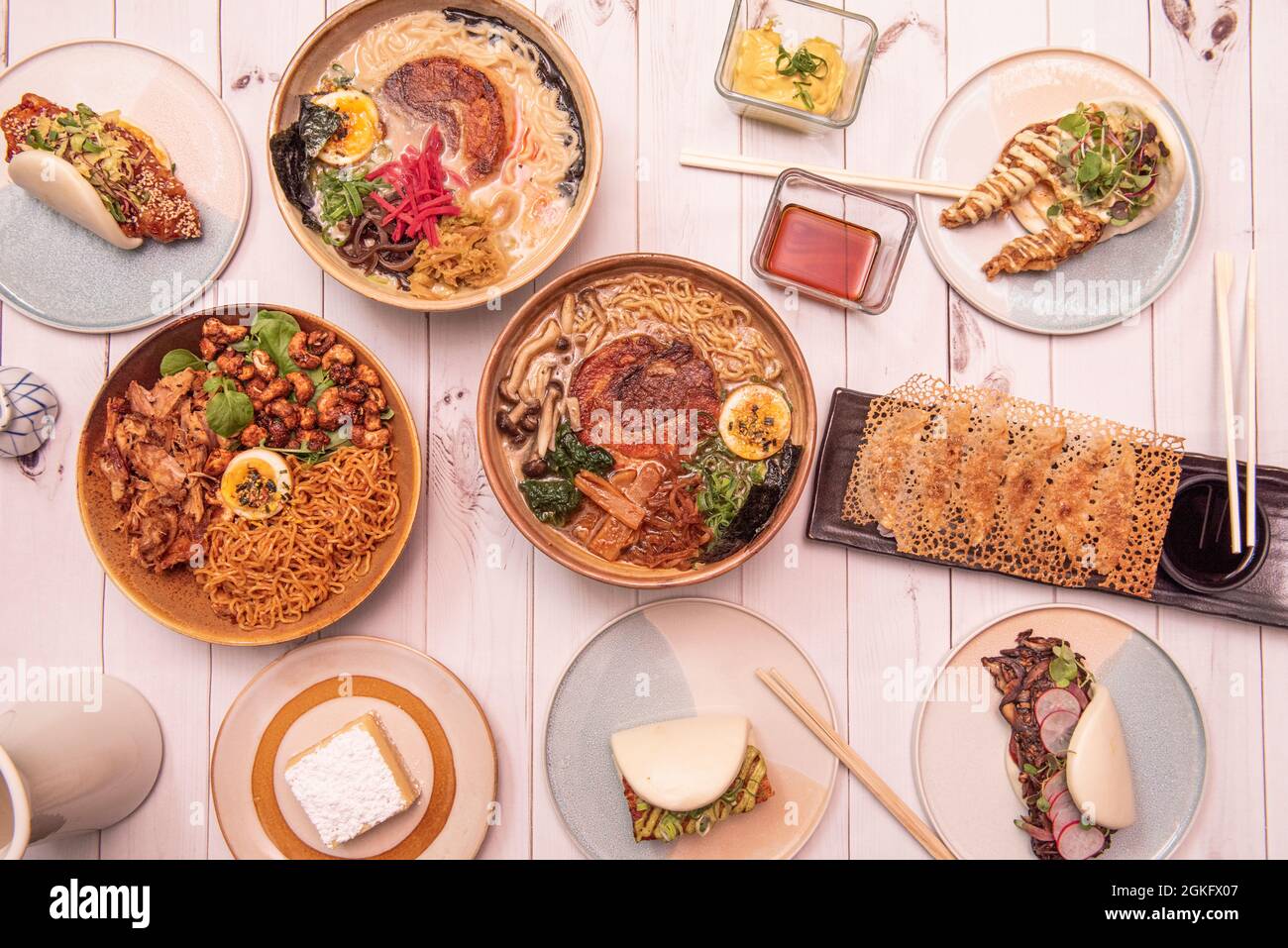 Teller mit typisch koreanischen und japanischen Speisen mit vielen Ramen, Nudeln, Gyozas, bao-Brot-Sandwiches, Krabben und Radieschen auf weißem Tisch Stockfoto