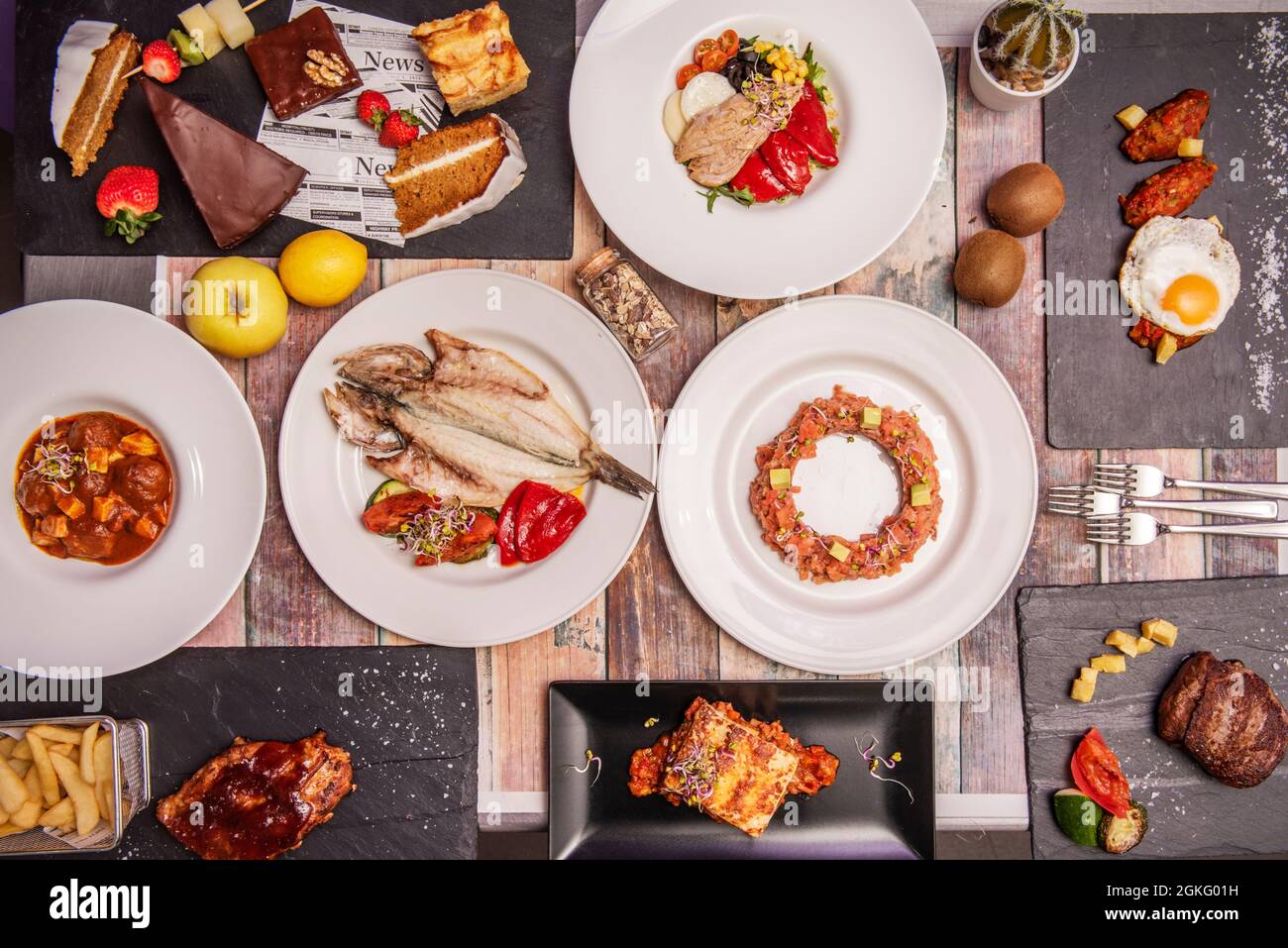 Draufsicht Bild von einem köstlichen Gericht aus spanischer Küche, gegrillte Goldbrasse, Schweinebacke, Hähnchenflügel mit Spiegelei, Lachstartare, Bauchsalat und Stockfoto
