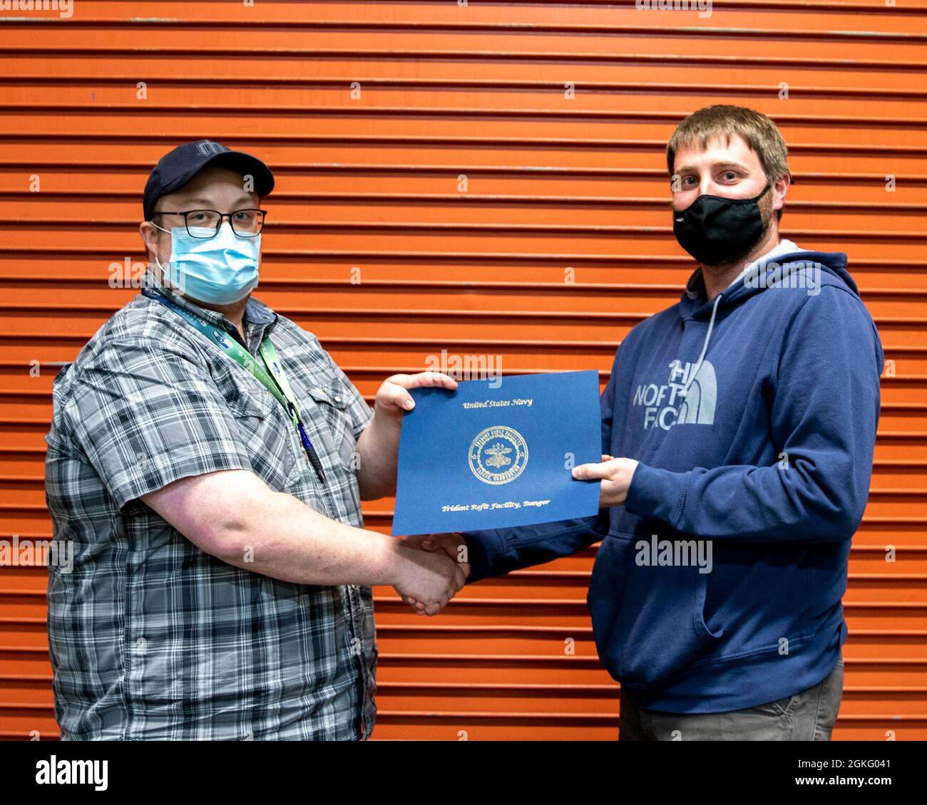 SILVERDALE, Washington (5. April 2021) – Ryan Reinke, General Foreman, Marine Machinist Shop, Trident Refit Facility Bangor (TRFB), überreicht Eric Simmons, Mechaniker, Marine Machinist Shop, am 5. April bei TRFB mit einem Incentive Award. Simmons arbeitete trotz schlechtem Wetter weiterhin auf fairwater-Flugzeugen. Stockfoto