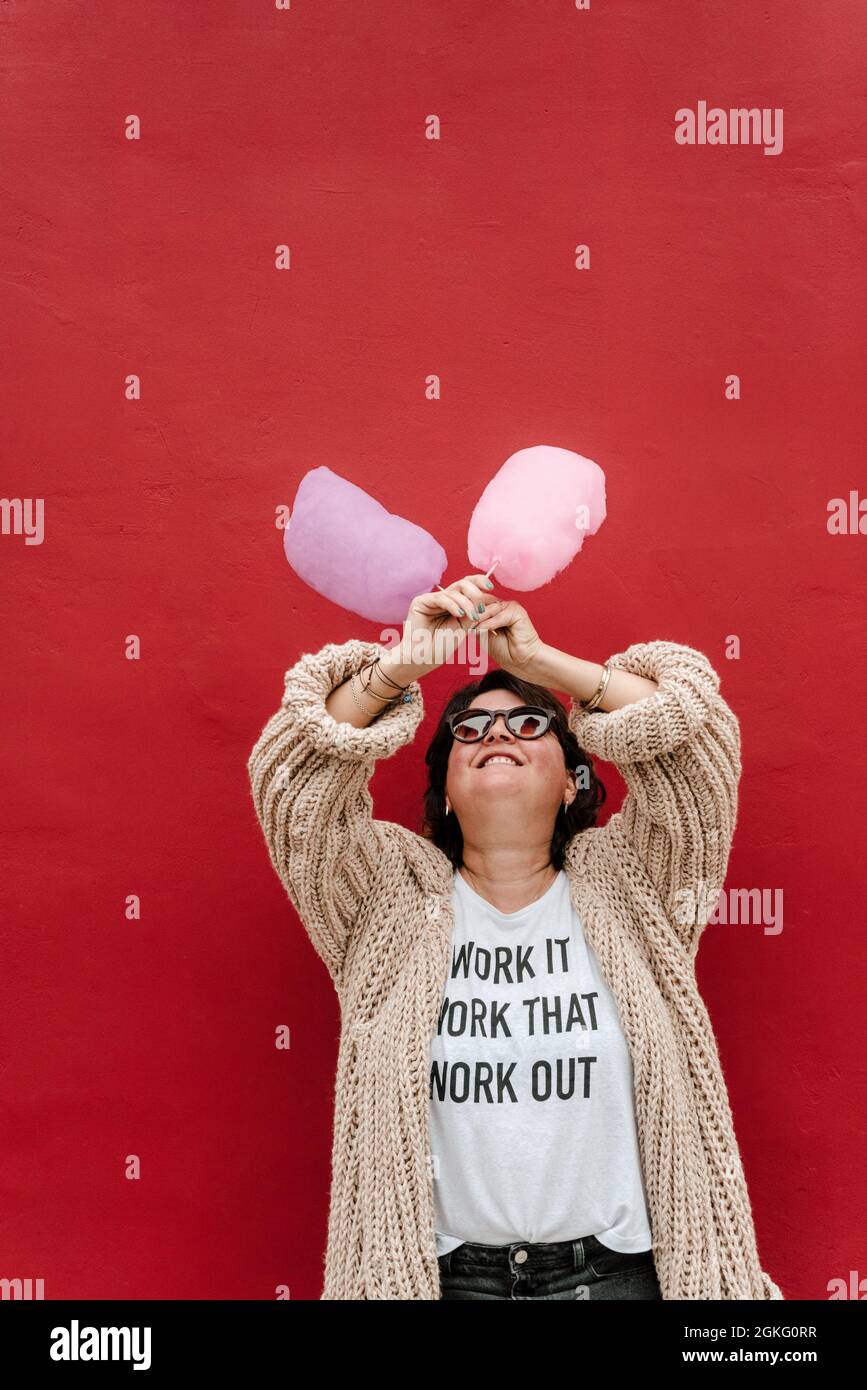 Lustiges Bild einer Frau, die ihre Arme mit zwei Zuckerwatte auf einem roten Hintergrund kreuzt. Speicherplatz kopieren Stockfoto