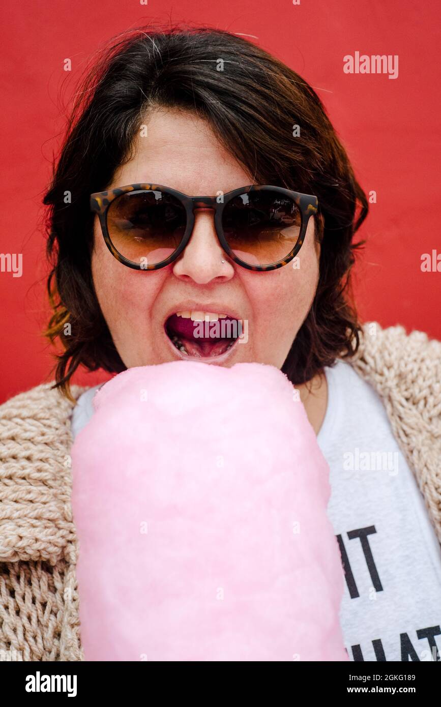 Porträt einer Frau, die gerade dabei ist, einen Bissen aus einer rosa Zuckerwatte zu nehmen. Tragen Sie dunkle Brille und kurze Haare Stockfoto