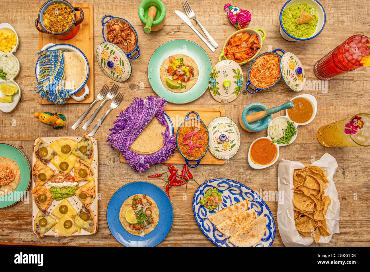 Bild der traditionellen mexikanischen Küche von oben auf einem hellen Holztisch. Gabeln, Cochinita pibil in einer Pfanne, synchronisierte Quesadillas, Mais Nachos, Mais Tortill Stockfoto