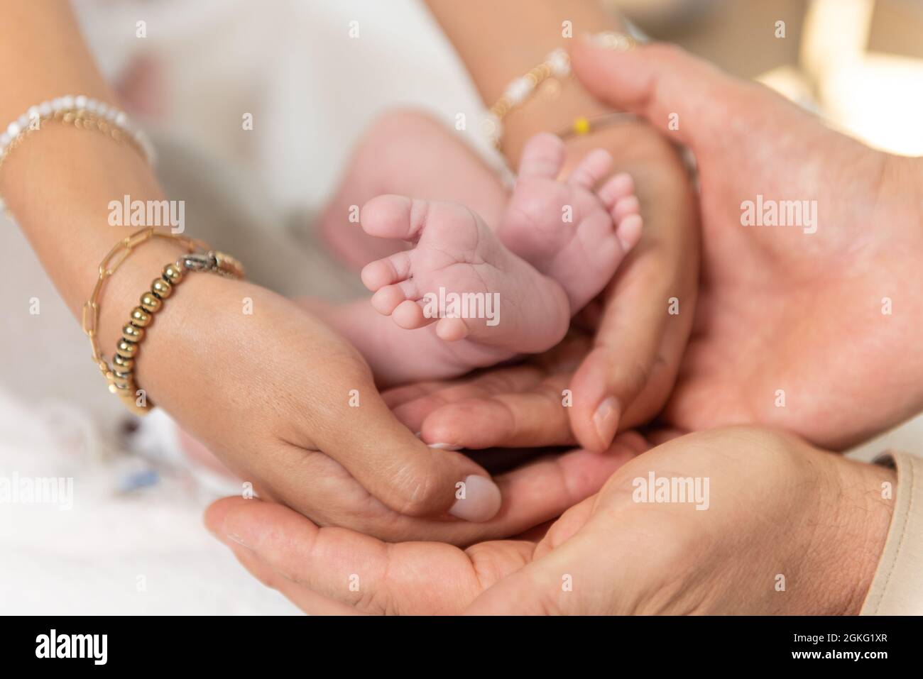 Kleine neugeborene Babyfüße, die von Mutter- und Vaterhänden gewogen werden, in einer Show des familiären Zusammengehörigkeitsgefühens Stockfoto