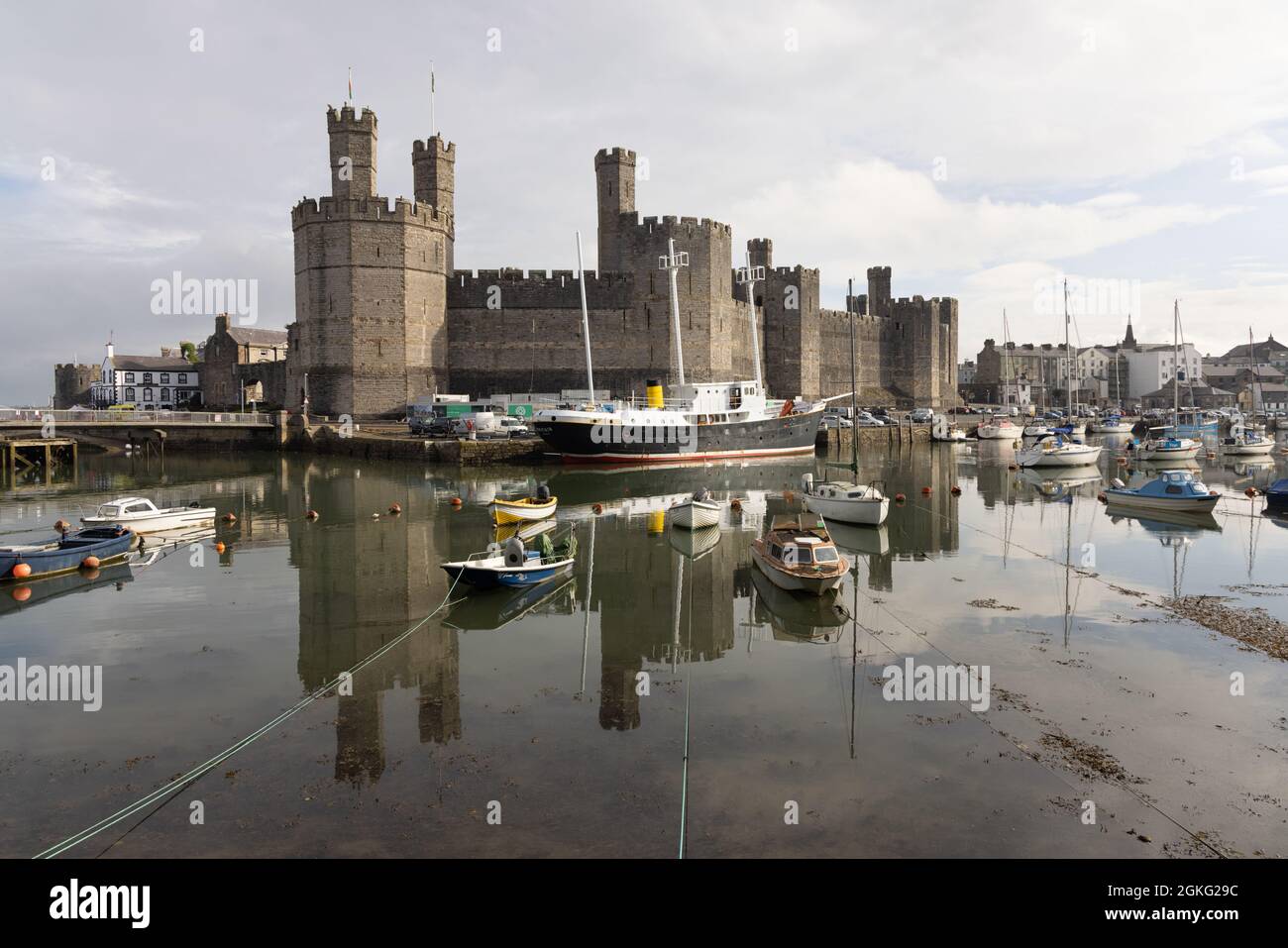 Caernarfon, Gwynedd, UK, 9. September 2021: Edward I. Schloss spiegelt sich im Hafen, in dem kleine Boote und Ex-Feuerschiff Großbritannien vertäut sind. Stockfoto