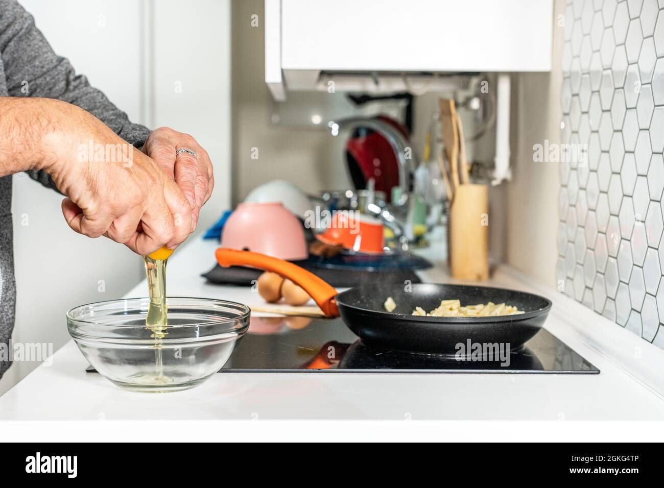 Die Hände des Mannes zerbrechen Eier, schlagen sie und mischen sie mit geschmorten Kartoffeln, um ein spanisches Omelett zuzubereiten Stockfoto