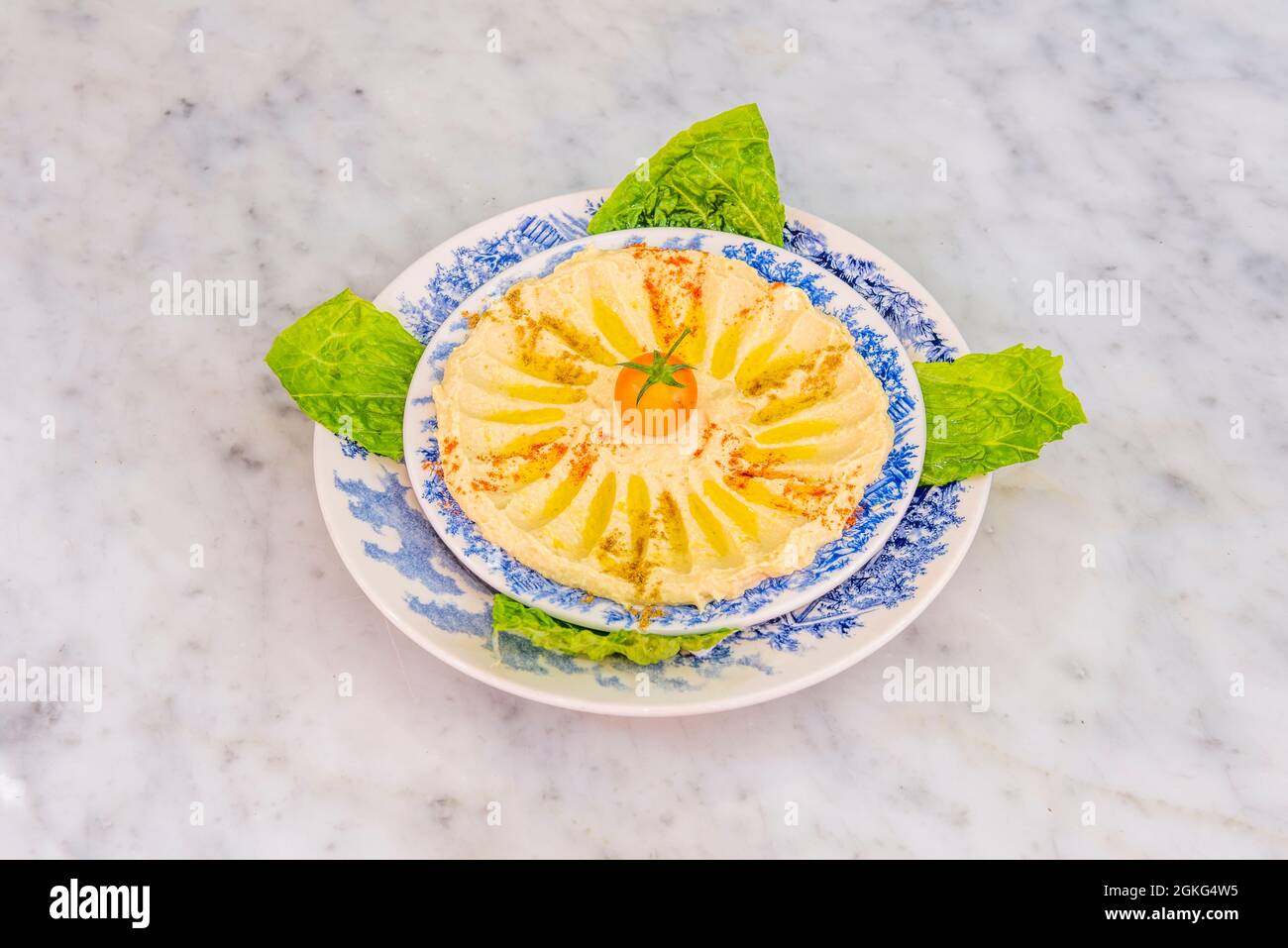 Kichererbsen-Hummus mit Olivenöl, Paprika, ras el Hanout und Kirschtomate und Salat zum Eintauchen auf Teller mit blauen Rändern Stockfoto