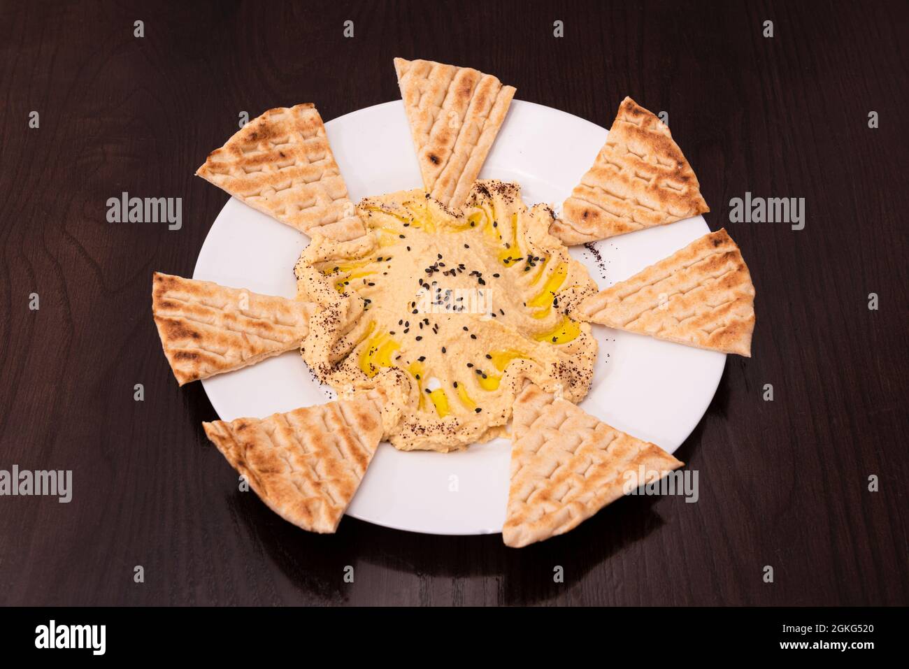 Kichererbsen-Hummus-Vorspeisen mit Olivenöl und ungesäuerten Brotscheiben zum Eintauchen auf einen Holztisch Stockfoto