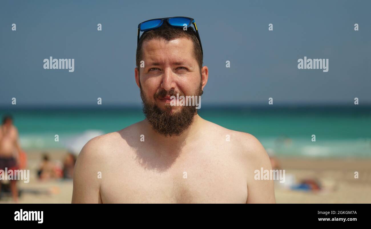 Ein authentisches Porträt eines jungen, selbstbewussten bärtigen Mannes, der die Kamera anschaut. Nahaufnahme eines jungen natürlichen Mannes am Strand. Stockfoto
