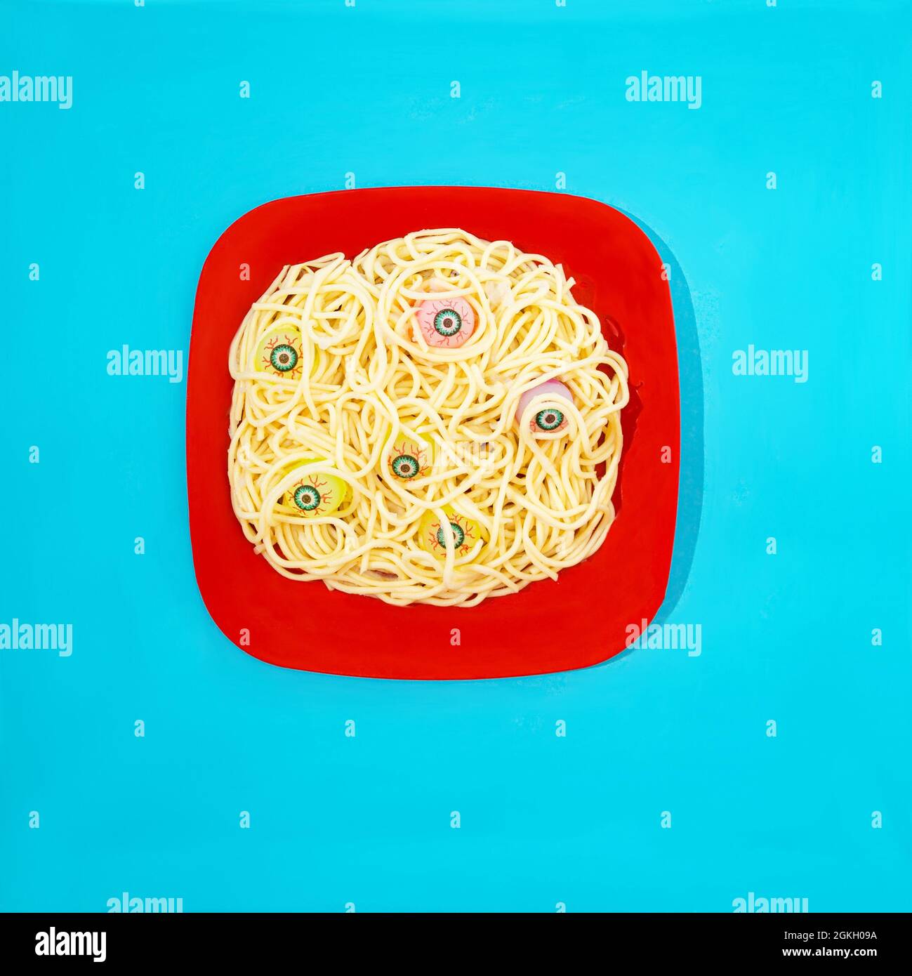 Ein roter Teller mit Spaghetti und gruseligen Augenkugeln, die aus dem Essen hervorgehen. Pastellblauer Hintergrund. Halloween Lunch oder Party Einladung kreatives Konzept. Stockfoto