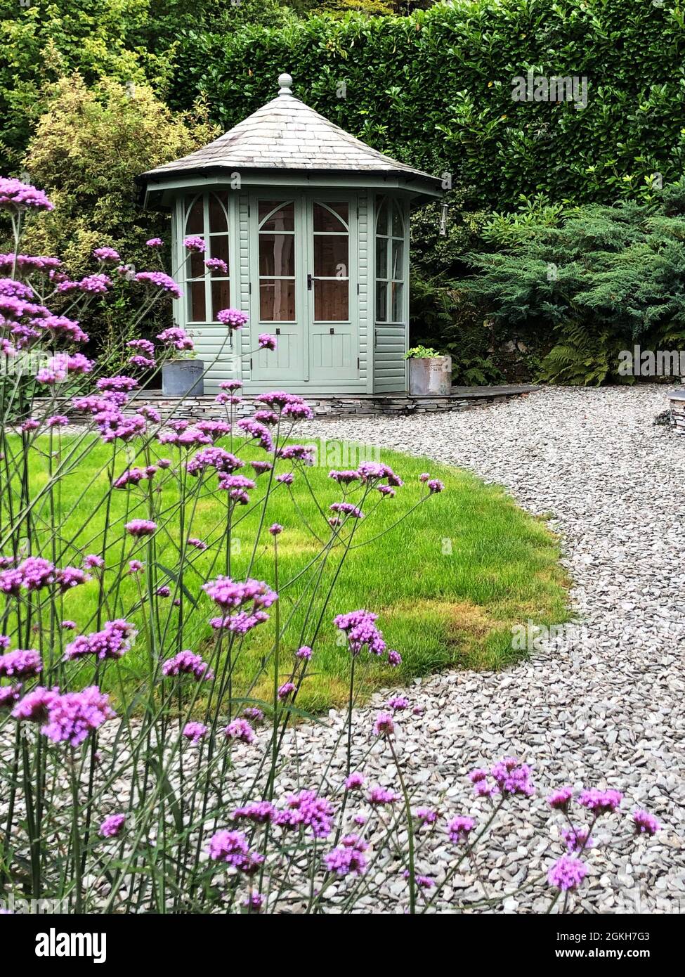 Ein malerisches Sommerhaus aus Holz in einem englischen Landschaftsgarten mit grünem Gras und Eisenkraut Blumen Stockfoto