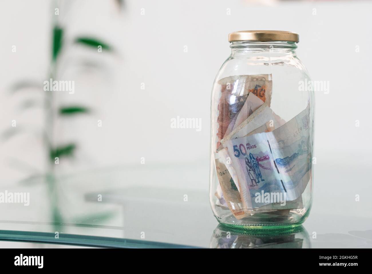 Geld, kolumbianische Banknoten im Glas, auf Glastisch, finanziell, Ersparnisse. Geldkassette, Glas voller Bargeld, Konzept der Einsparung von Geld, Planung und Kontro Stockfoto