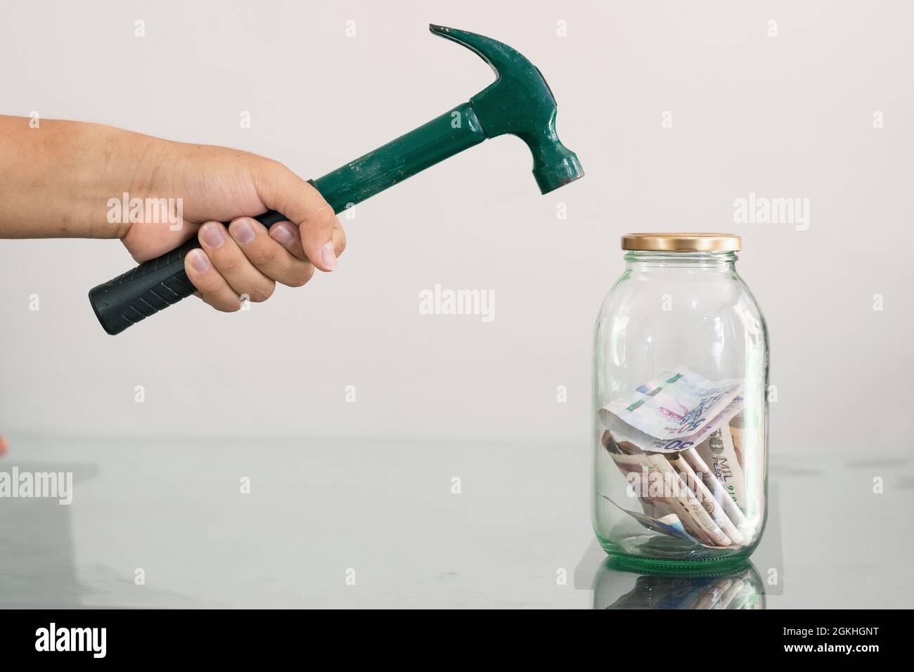Mann mit Hammer in der Hand brechen Sparschwein. Glas mit Banknoten, Ersparnisse und persönliche Finanzen. Weißer Hintergrund. Wirtschaftskonzept Stockfoto