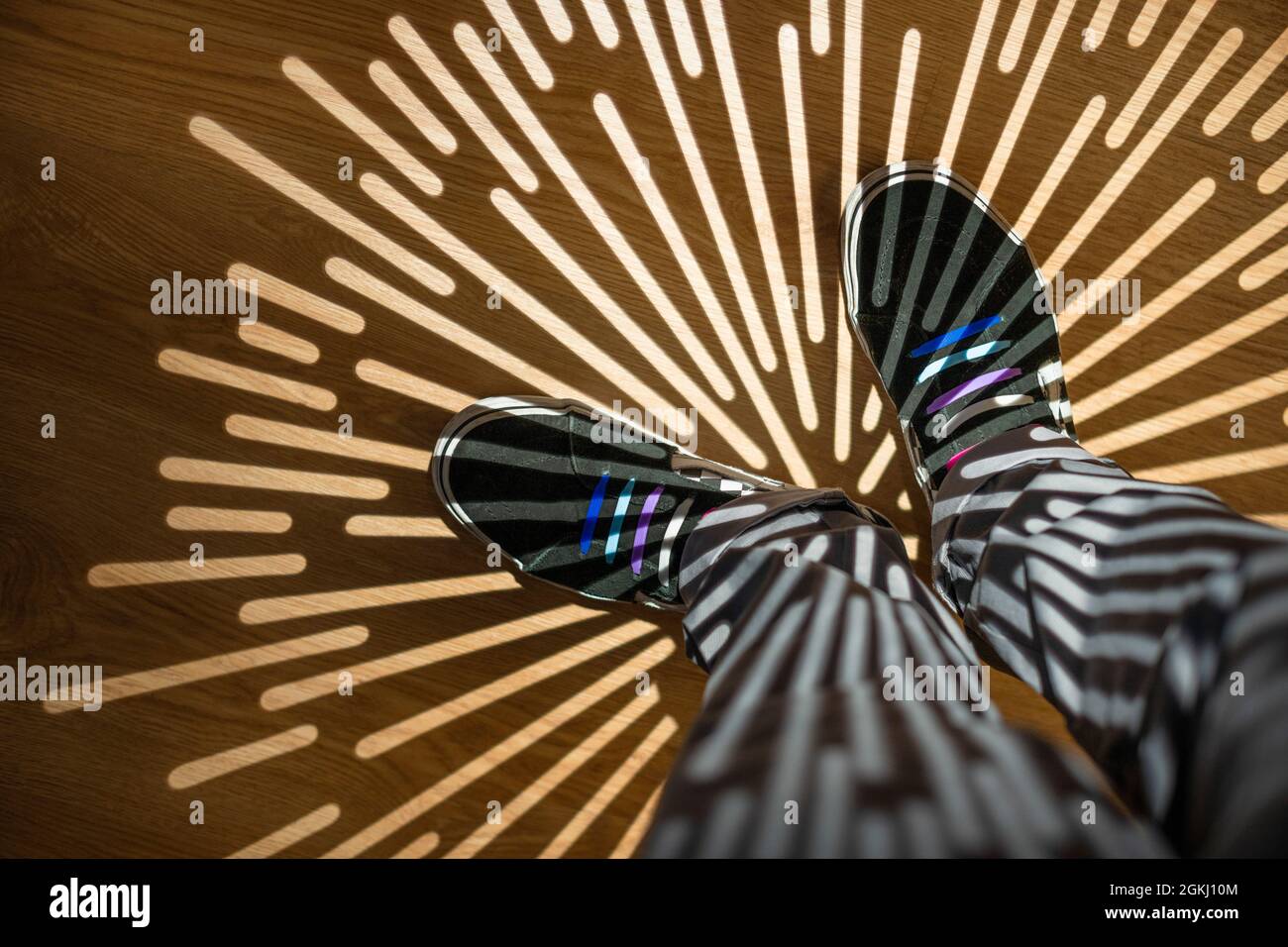 Sternförmige Schatten auf den Beinen mit grauer Hose und schwarzen Sneakers mit farbigen Schnürsenkeln Stockfoto