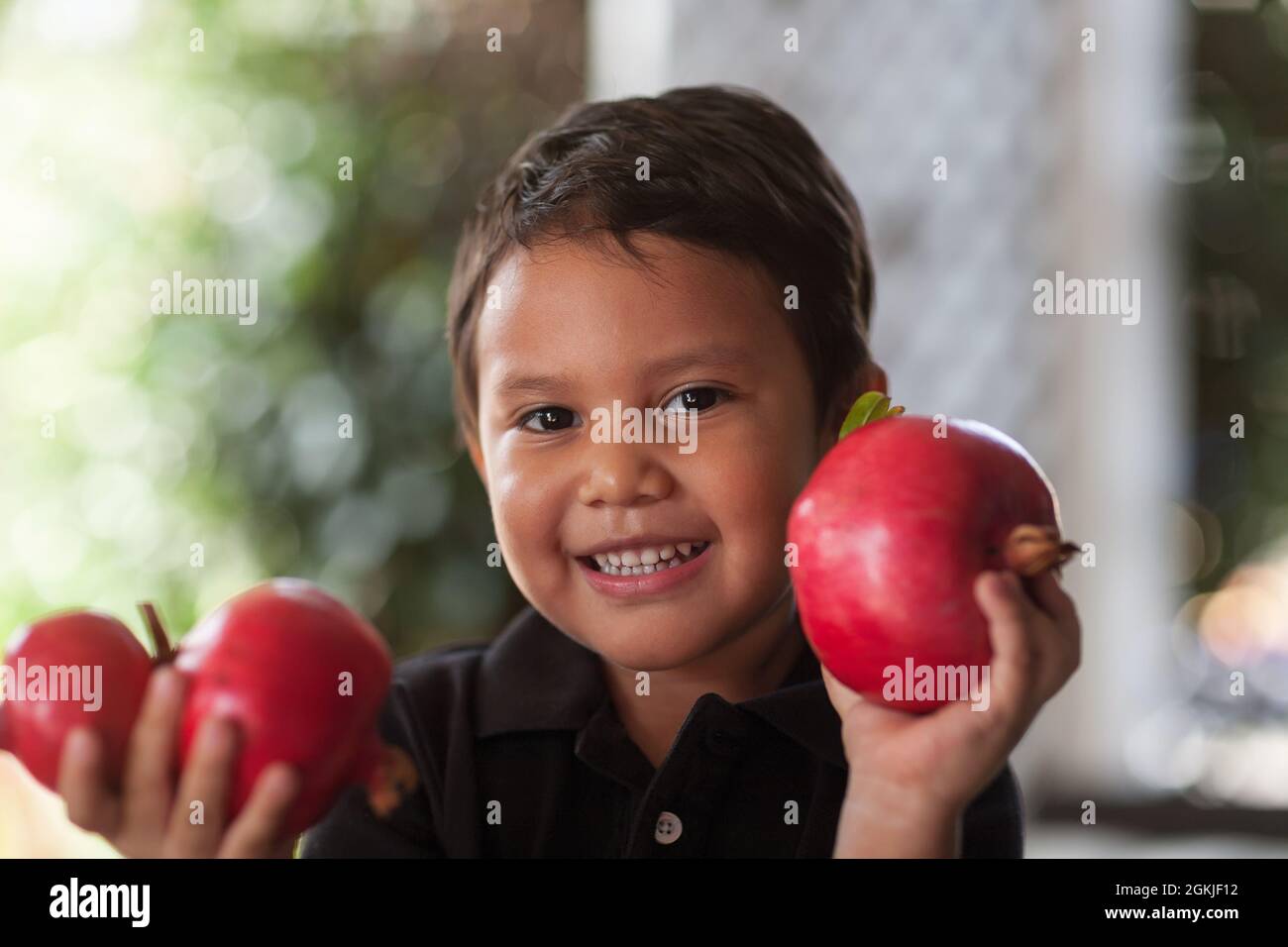 Lächelndes Kind hält in seinen kleinen Händen frisch geschnittene Granatäpfel, die biologisch angebaut werden. Stockfoto