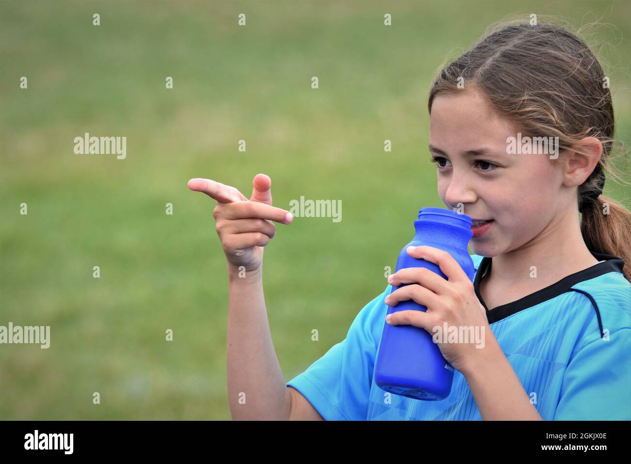 Das 9-jährige Mädchen trank während der Halbzeit ihres ersten Fußballmatches Flüssigkeit und zeigte auf die gegnerische Mannschaft, die sie verloren hatten, um den Leertext zu kopieren Stockfoto