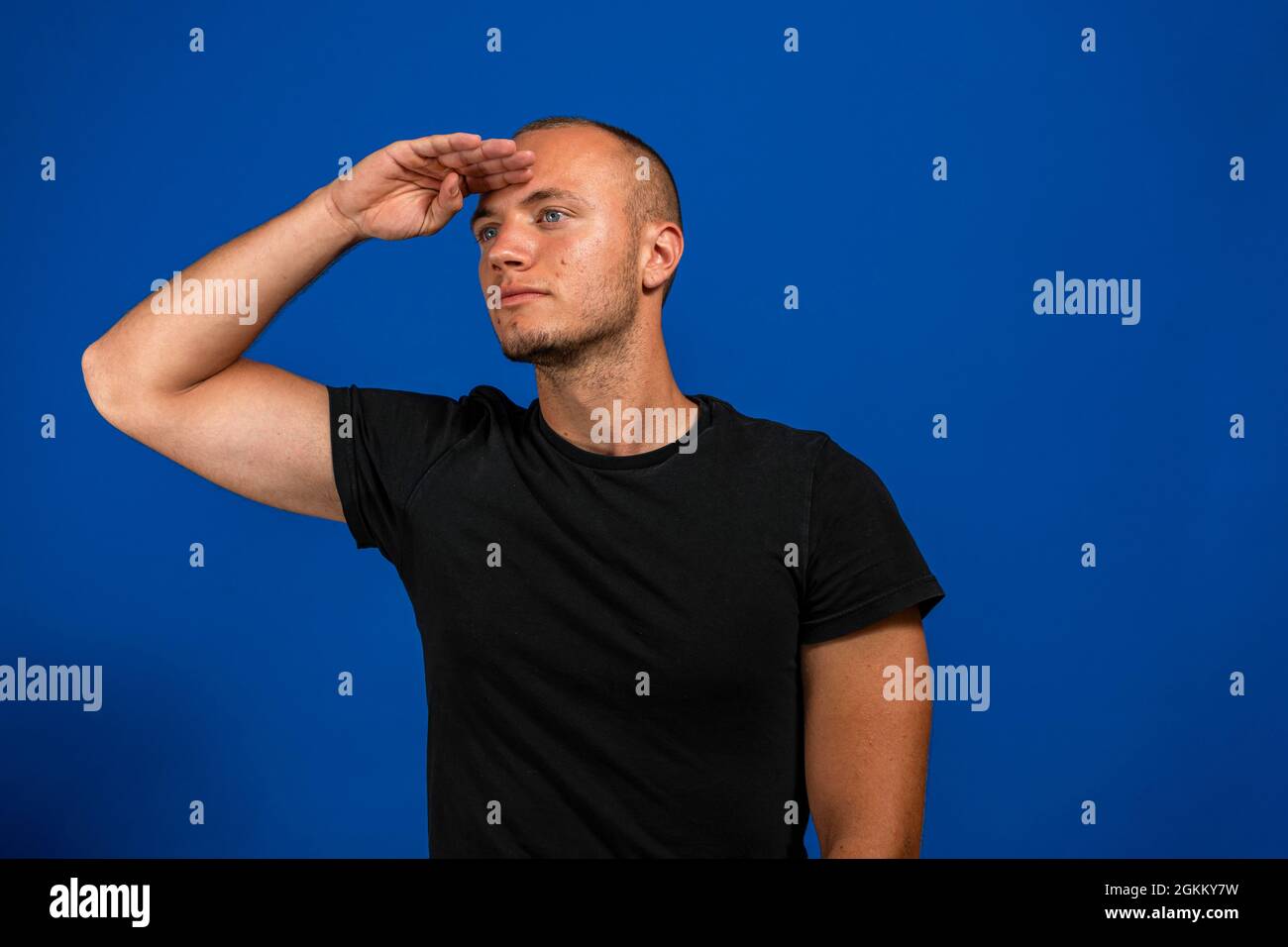 Der junge Mann begrüßt die Kamera mit einem militärischen Gruß in einem Akt der Ehre und des Patriotismus und zeigt Respekt vor der blauen Wand Stockfoto