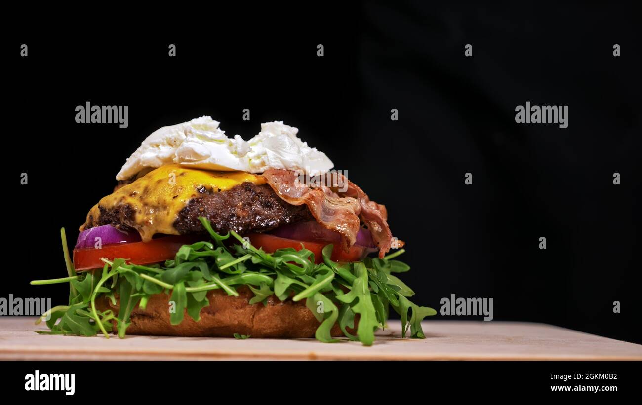 Handwerk Burger ist Kochen auf schwarzem Hintergrund. Bestehen: sauce, Rucola, Tomaten, roten Zwiebeln, Speck, rote Johannisbeeren Sauce, ricotta Cottage frischen Käse, Luft b Stockfoto
