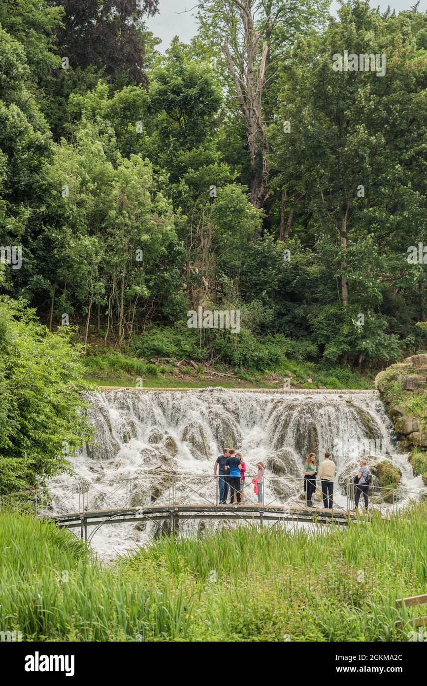Gruppe von Menschen, die auf einer kunstvollen Brücke mit Blick auf einen großen Wasserfall in den Gärten des Blenheim Palace Oxfordshire England UK stehen Stockfoto