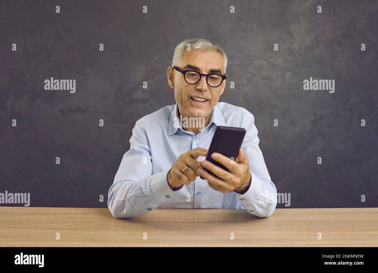 Ein lächelnder älterer Mann schreibt über ein modernes Mobiltelefon Nachrichten oder durchsucht Nachrichten im Internet. Stockfoto