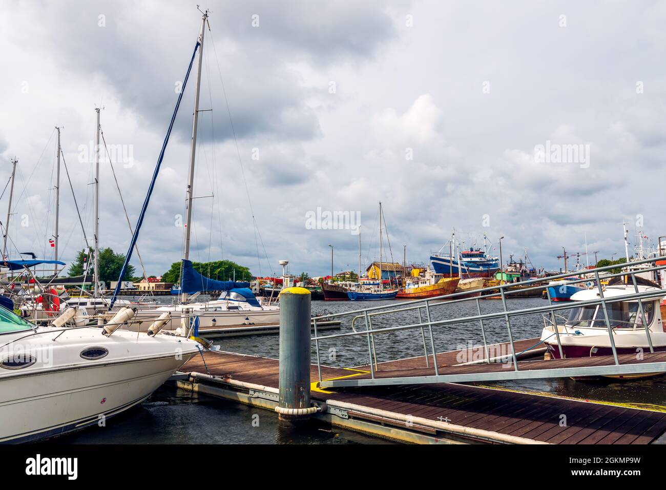 Hafen an der Ostsee in Darłówko, Polen. Segelboote und Angelscheren, die auf einer Wasseroberfläche schwimmen. Sommer, bewölkt, windiger Tag. Holzsteg und Farbgebung Stockfoto