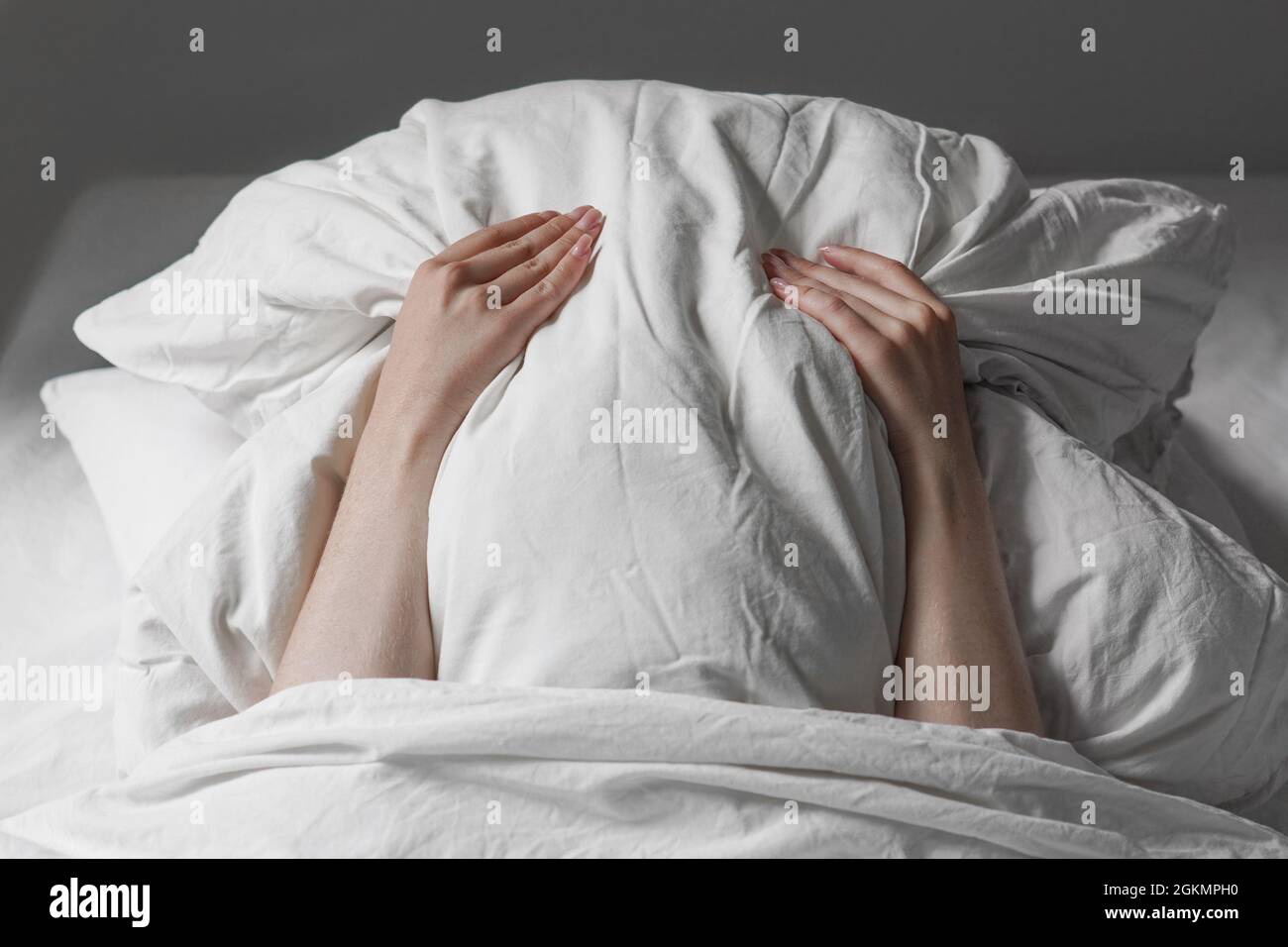 Frau im Bett versteckt Gesicht unter Kissen Stockfoto