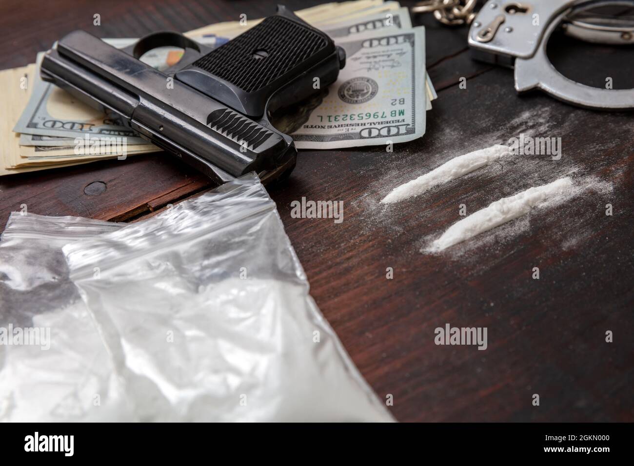 Drogenschmuggel und -Handel, Handschellen, Pistolengeld und Kokainpakete auf Holztischhintergrund. Handel mit illegalen Substanzen und Verhaftung Stockfoto