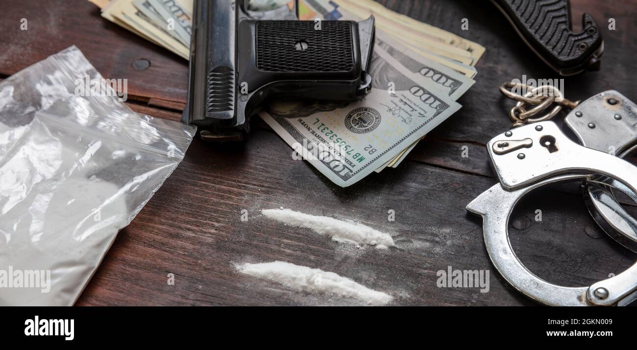Drogen Substanzen illegale Geschäfte und Festnahmen. Handschellen, Pistolengeld und Kokainpakete auf Holztischhintergrund. Schmuggel und Menschenhandel Stockfoto