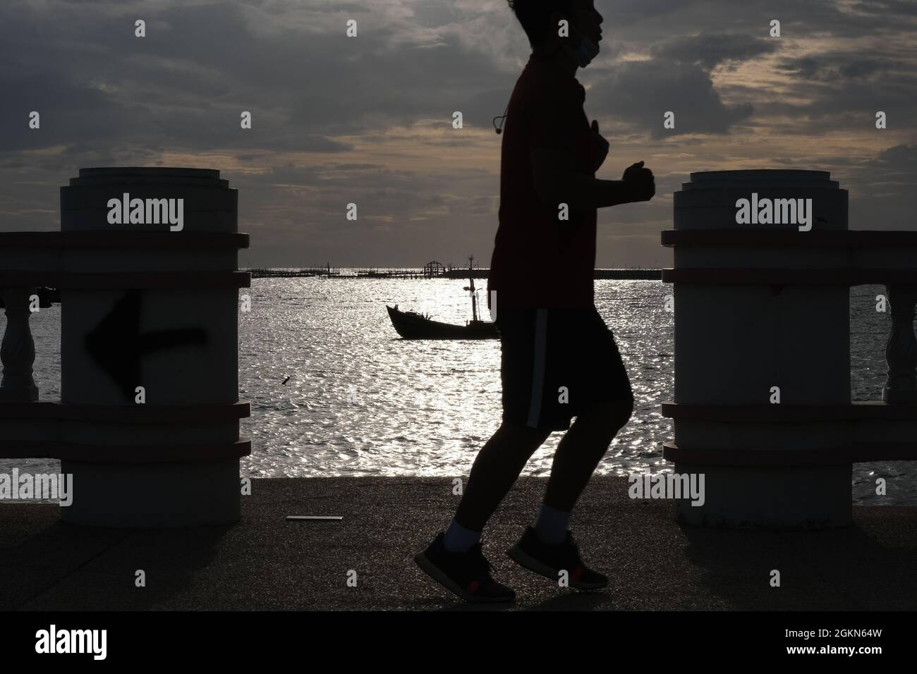 Eine Silhouette eines Mannes, der gegen das sonnenbeschienenen Meer joggt Stockfoto