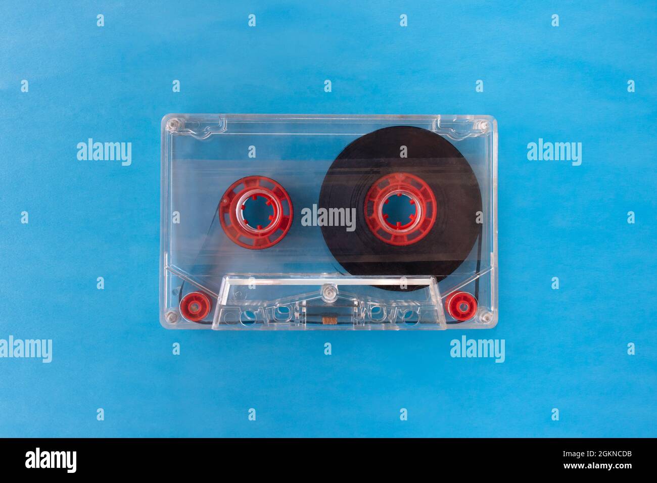 Eine transparente, kompakte Audiokassette mit sichtbarem Klebeband und roten inneren Rollen, isoliert auf blauem Hintergrund. Draufsicht flach liegend mit Platz für Text Stockfoto