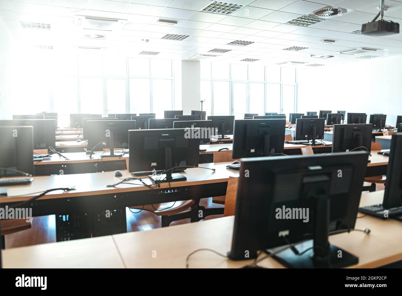 Leeres Großraumbüro mit mehreren Arbeitsplätzen mit Desktop-Computern in einem modernen Büro, einer Hochschule oder einem Callcenter mit Blick auf helle Fenster und Stockfoto